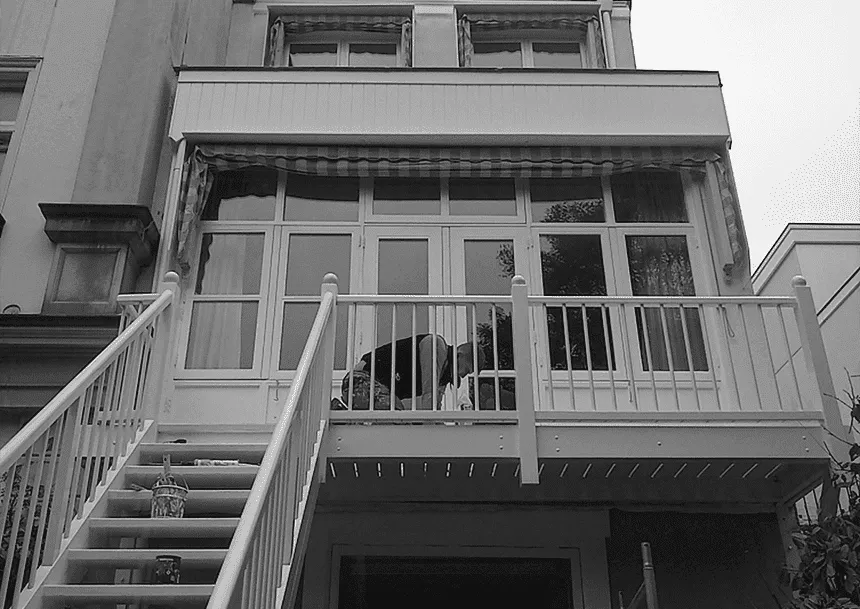 Wit geschilderde veranda met balustrade en buitentrap aan de Zeestraat in Den Haag, met een schilder aan het werk
